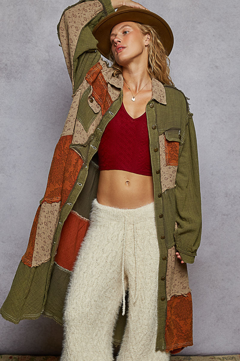 Person wearing a patchwork coat with a red top and white pants against a gray background