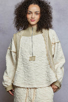 Person wearing a beige quilted jacket and pants against a gray background