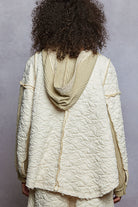 Person wearing a textured cream jacket with a hood against a gray background