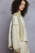 Woman wearing a textured white coat with a beige scarf against a gray background