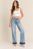 Light-wash wide-leg jeans with a high-rise waist, classic five-pocket design, subtle fading, and darker frayed cuffed hems, styled with a white ribbed crop top and white block-heel sandals.