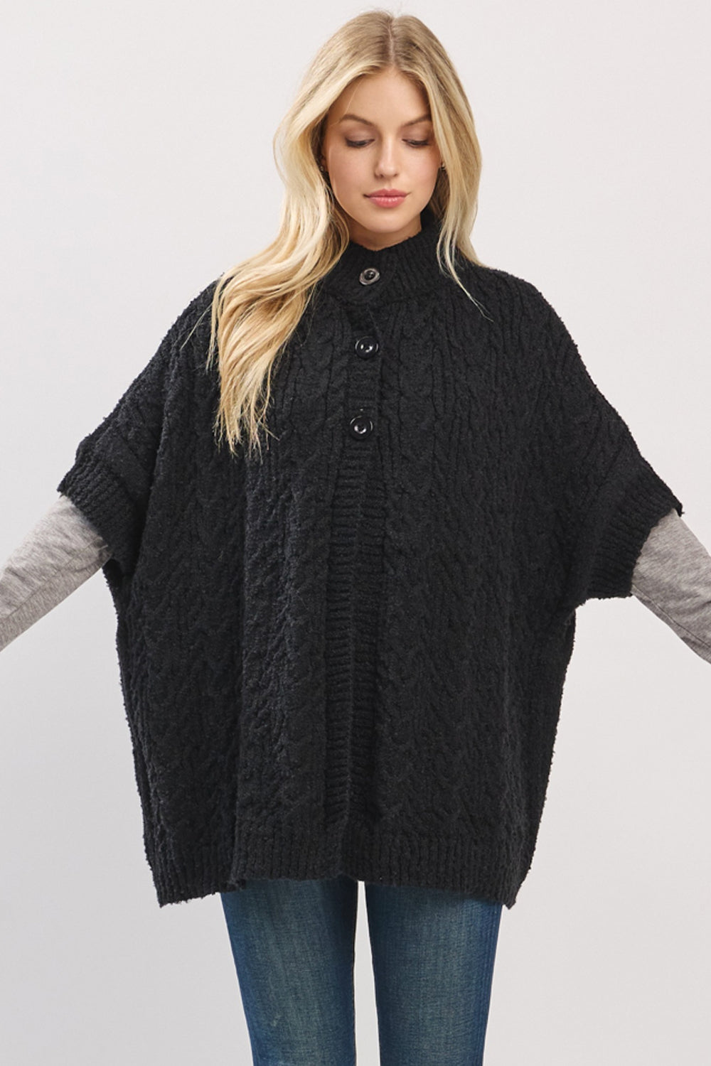 Woman wearing a black cable knit poncho over a gray sweater on a light gray background