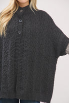 Dark gray cable knit poncho worn by a person on a light gray background