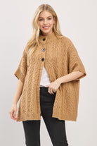 Woman wearing a brown cable knit poncho on a white background
