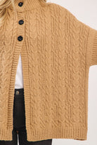 Close-up of a beige cable knit cardigan with black buttons on a white background
