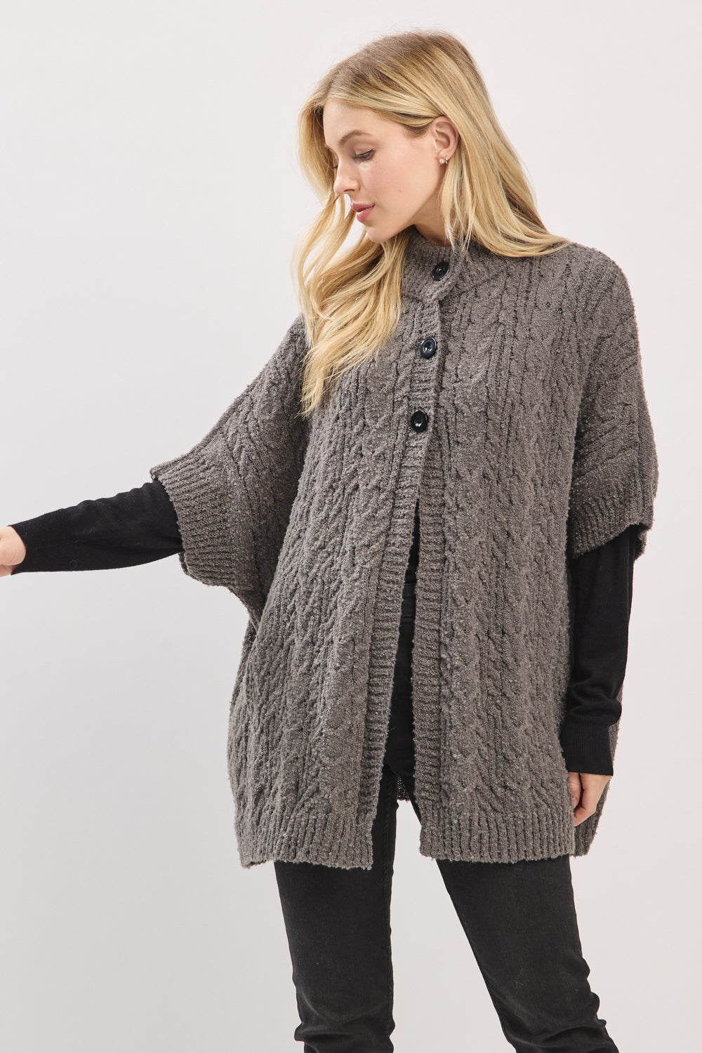 Woman wearing a gray cable knit poncho on a white background