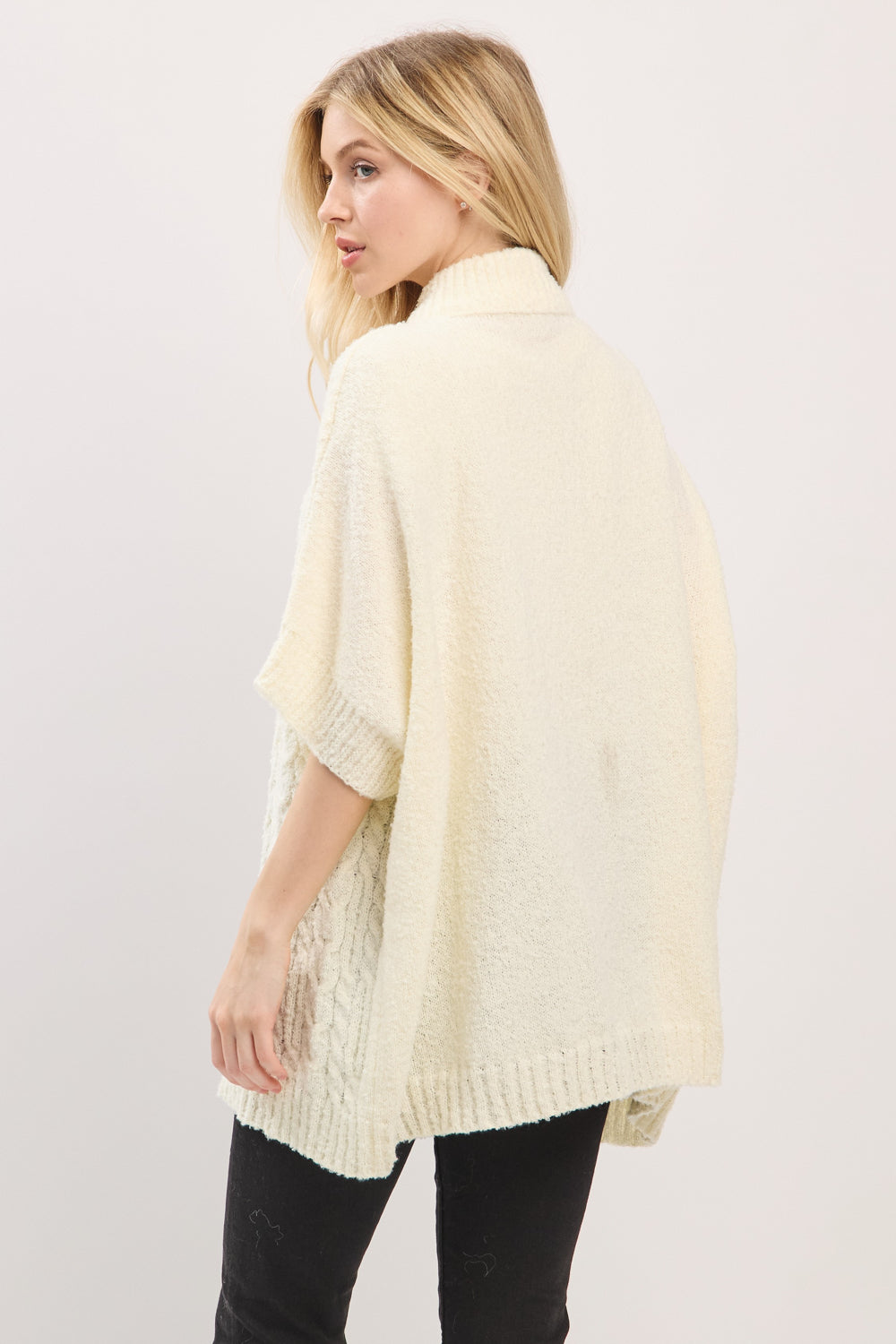 Woman wearing a light yellow knitted poncho against a white background