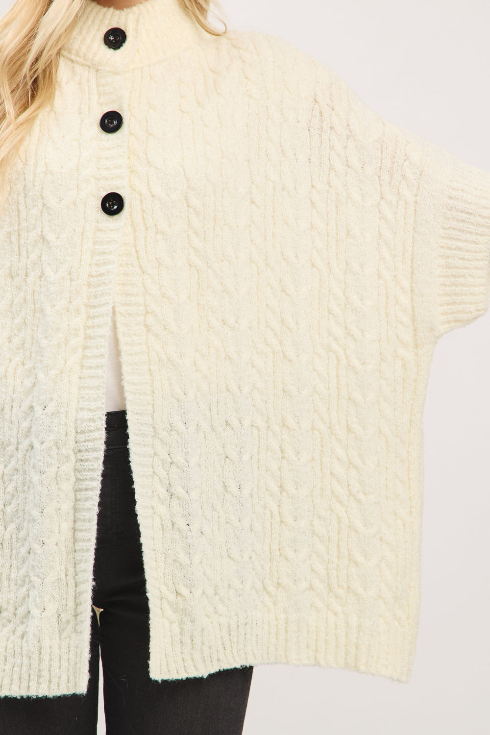 Close-up of a cream-colored knitted cardigan with black buttons on a plain background